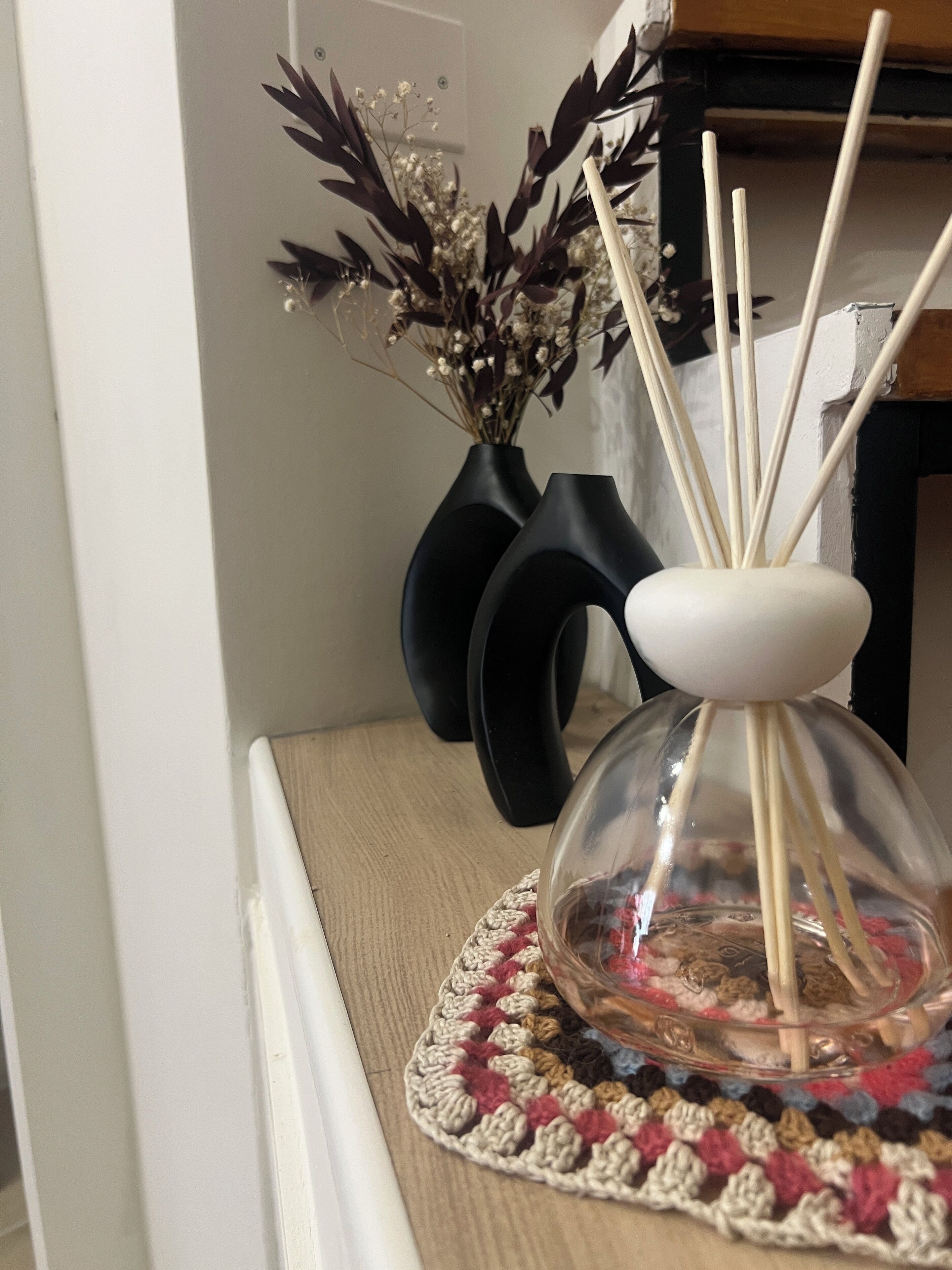 Een glazen diffuser met rietstokjes op een geweven onderzetter, geplaatst op een houten oppervlak.