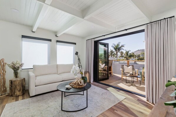 A modern living room with a sofa, coffee table, and a view of the outdoors through large sliding glass doors.