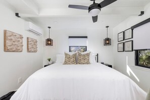 A bedroom with a large bed, a ceiling fan, wall-mounted lights, and a window with a view.