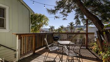 A deck with outdoor furniture, a grill, and a view of palm trees and mountains.