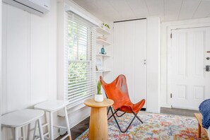 Ein Zimmer mit Fenster, Stuhl, kleinem Tisch und Tür.