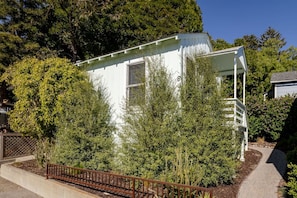 A white building with a porch, surrounded by dense greenery and trees. - The Pine House — Dog Friendly Studio with Ocean View Deck | Queen Bed Under the Pines · In-Unit Washer & Dryer · AC · Full Kitchenette · Beach Gear & Bikes · Avila Beach · Sleeps 2 · Managed by Solmaré Stays (Avila Beach)