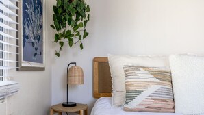 Ein Schlafzimmer mit einem Bett, einer hängenden Pflanze, einer Lampe und einem gerahmten Bild an der Wand.