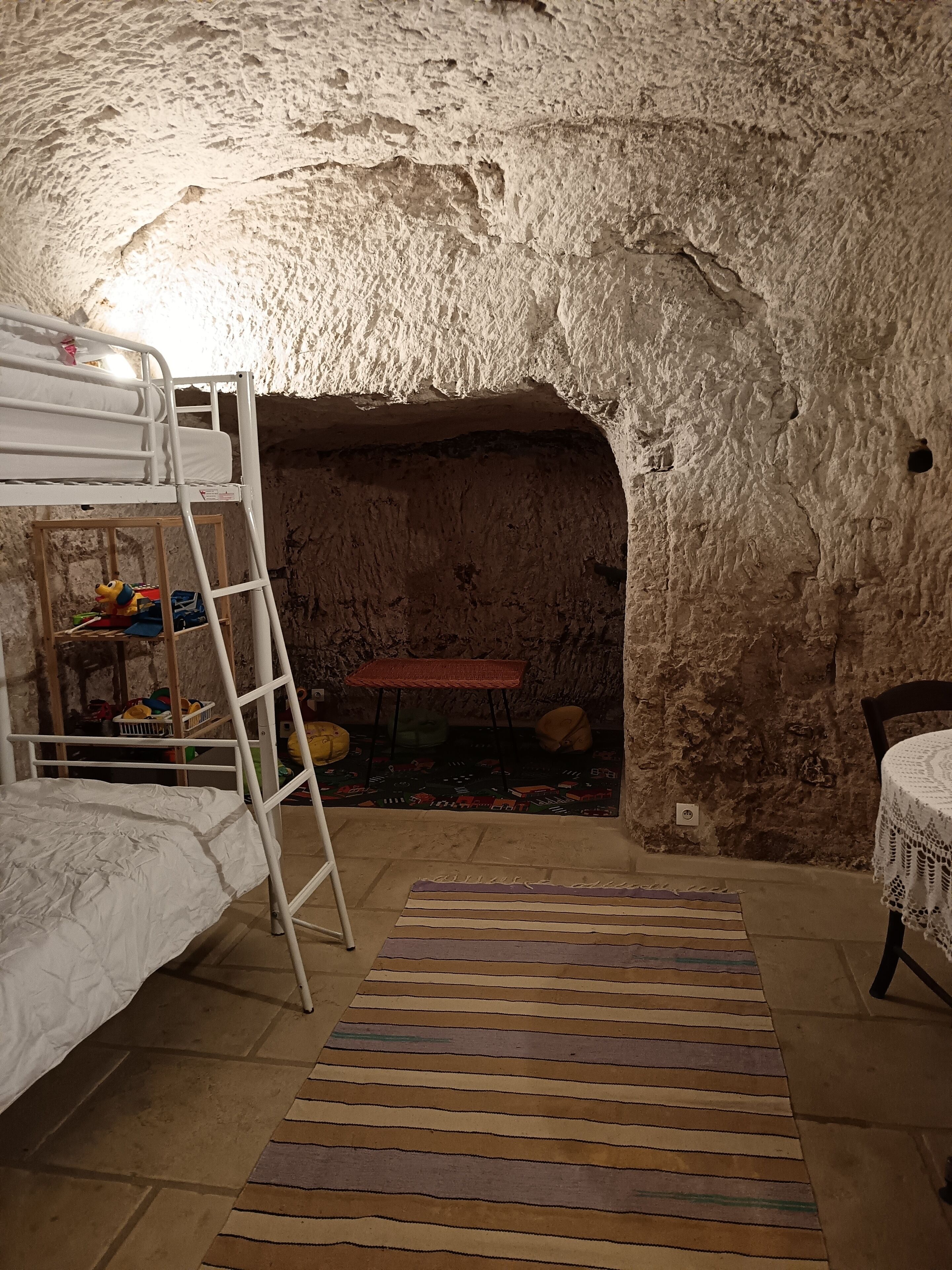 Een grotachtige kamer met stapelbedden, een klein tafeltje en een kamerkleed met een patroon.