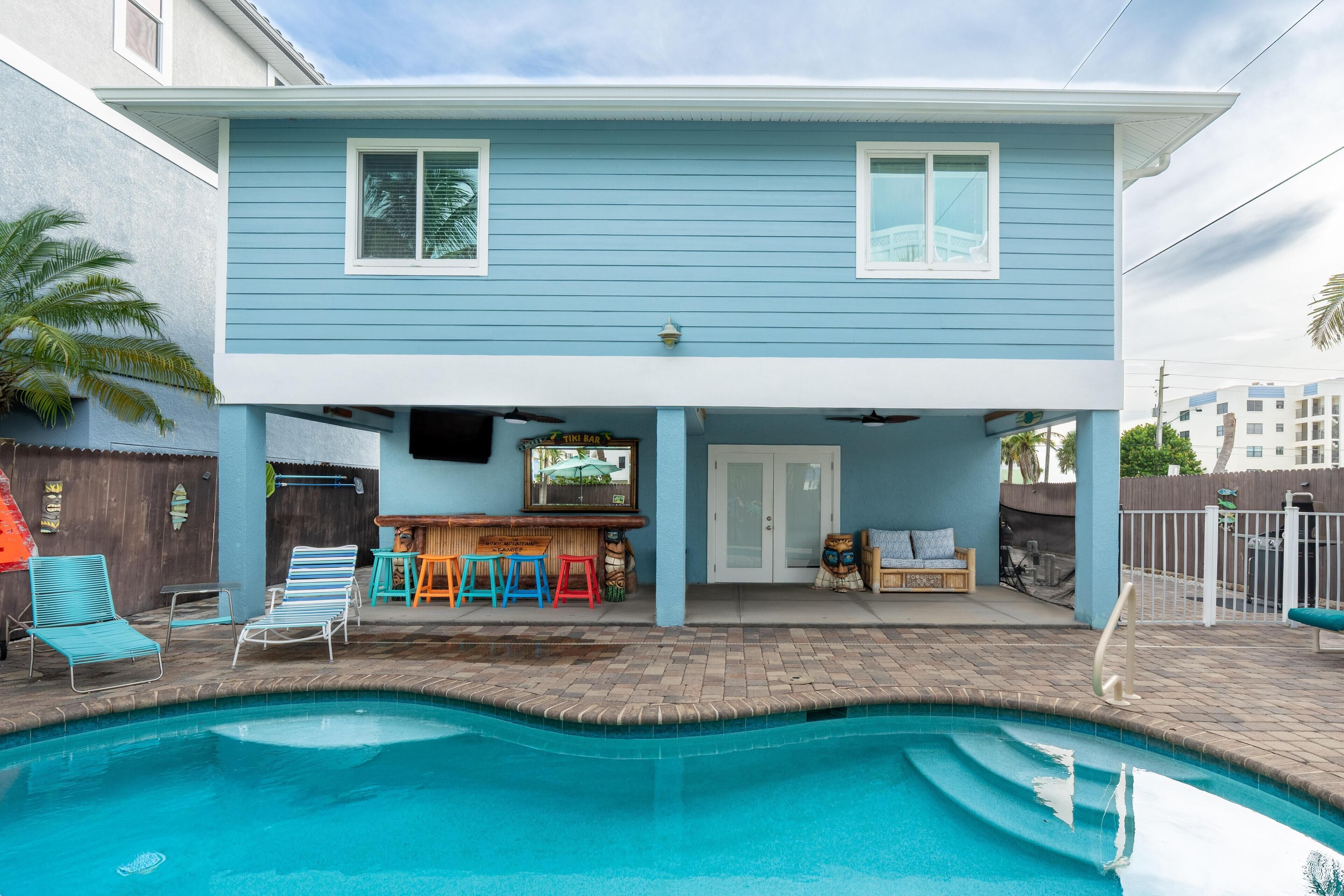 A two-story house with a pool, outdoor seating, and a tiki bar.