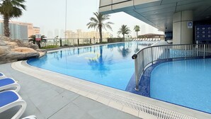Une piscine avec des chaises longues, un panneau indiquant qu’il est interdit de se baigner, et une vue sur un paysage urbain avec des immeubles.