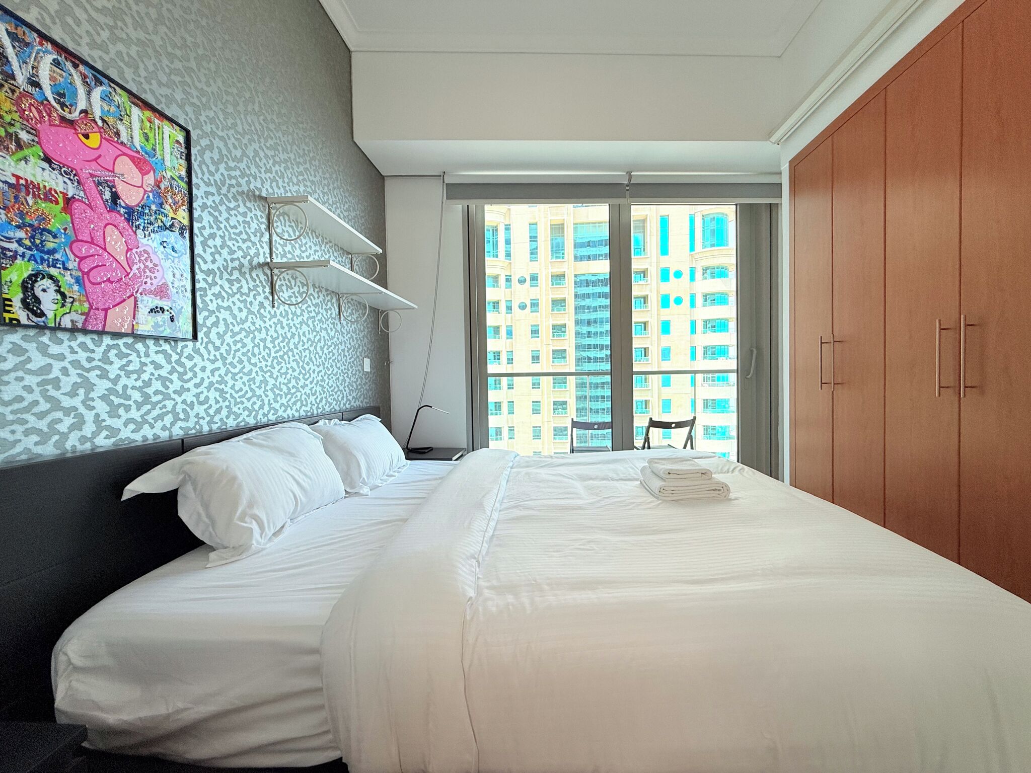 Une chambre d’hôtel avec un grand lit, une vue sur de hauts immeubles, une armoire et un tableau au mur.