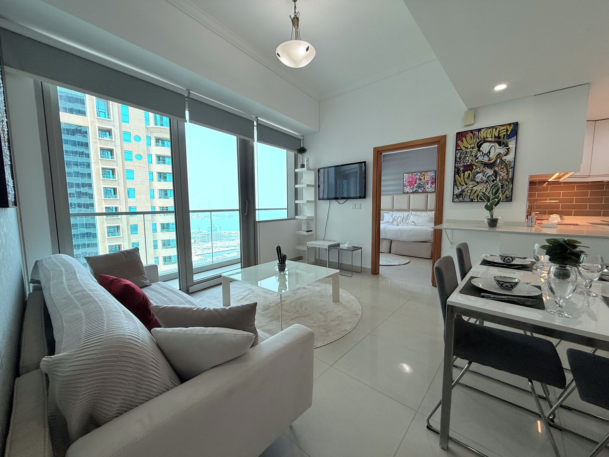 A modern apartment with a living room, dining area, and bedroom. It features large windows, a flat-screen TV, and a dining table set for four.