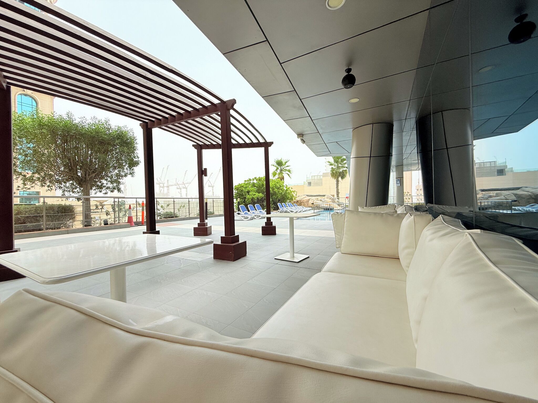 A modern lounge area with a white sofa, a pergola, and a pool view.