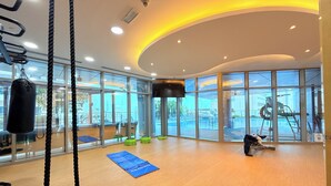 Une salle de sport spacieuse, dotée de grandes fenêtres, d’un sac de frappe et d’un tapis bleu sur le sol.