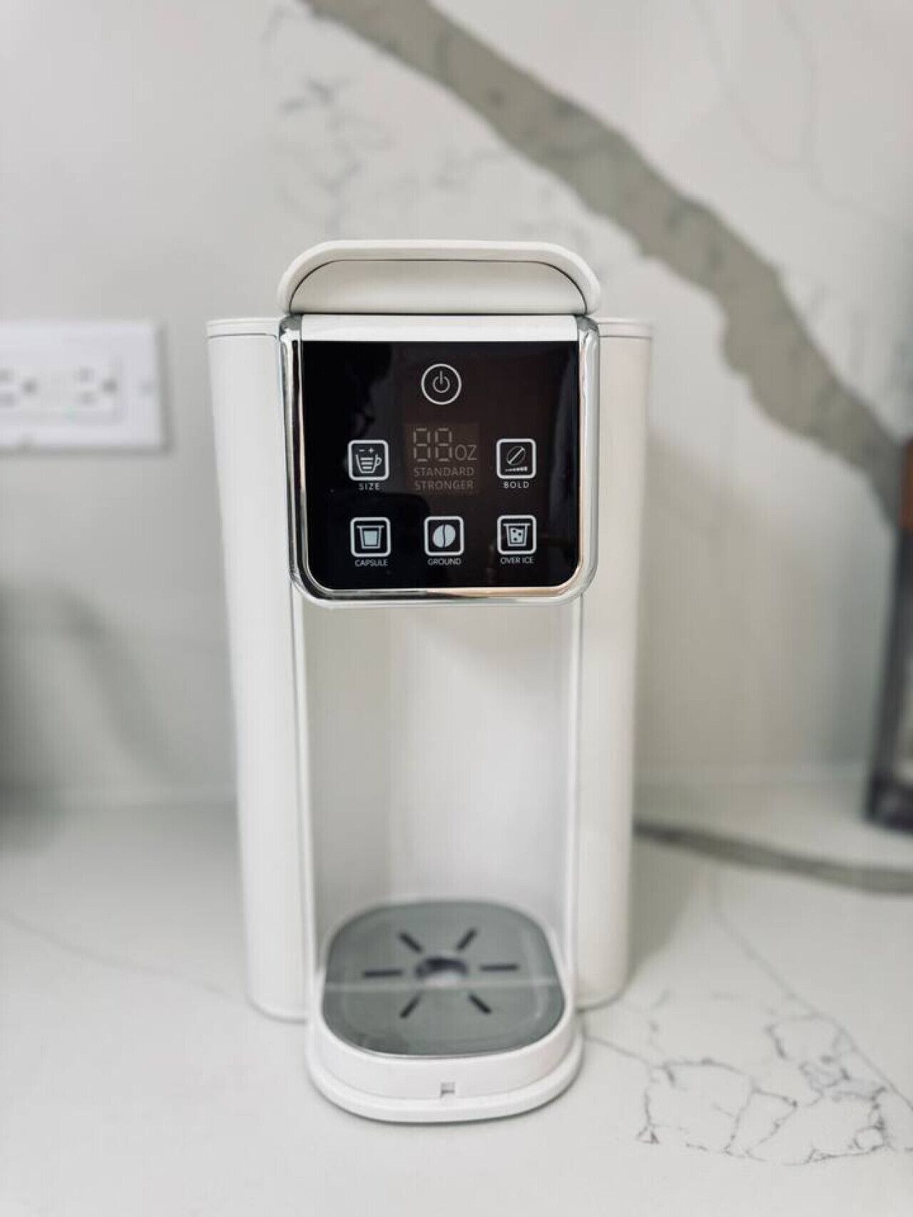 A white coffee machine with a digital display on a marble countertop.