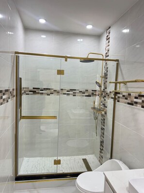 A modern bathroom with a glass-enclosed shower, white tiles, and a gold shower head. - Modern Beach Retreat Near Puerto Seco, Dunn`s River and Plantation Cove (St Anns Bay P O)