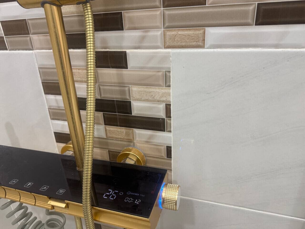 A modern shower with a digital display, a gold hose, and a control panel.