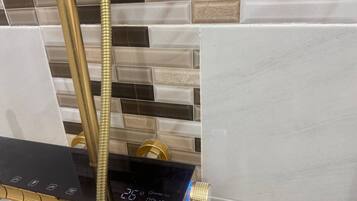 A modern shower with a digital display, a gold hose, and a control panel.