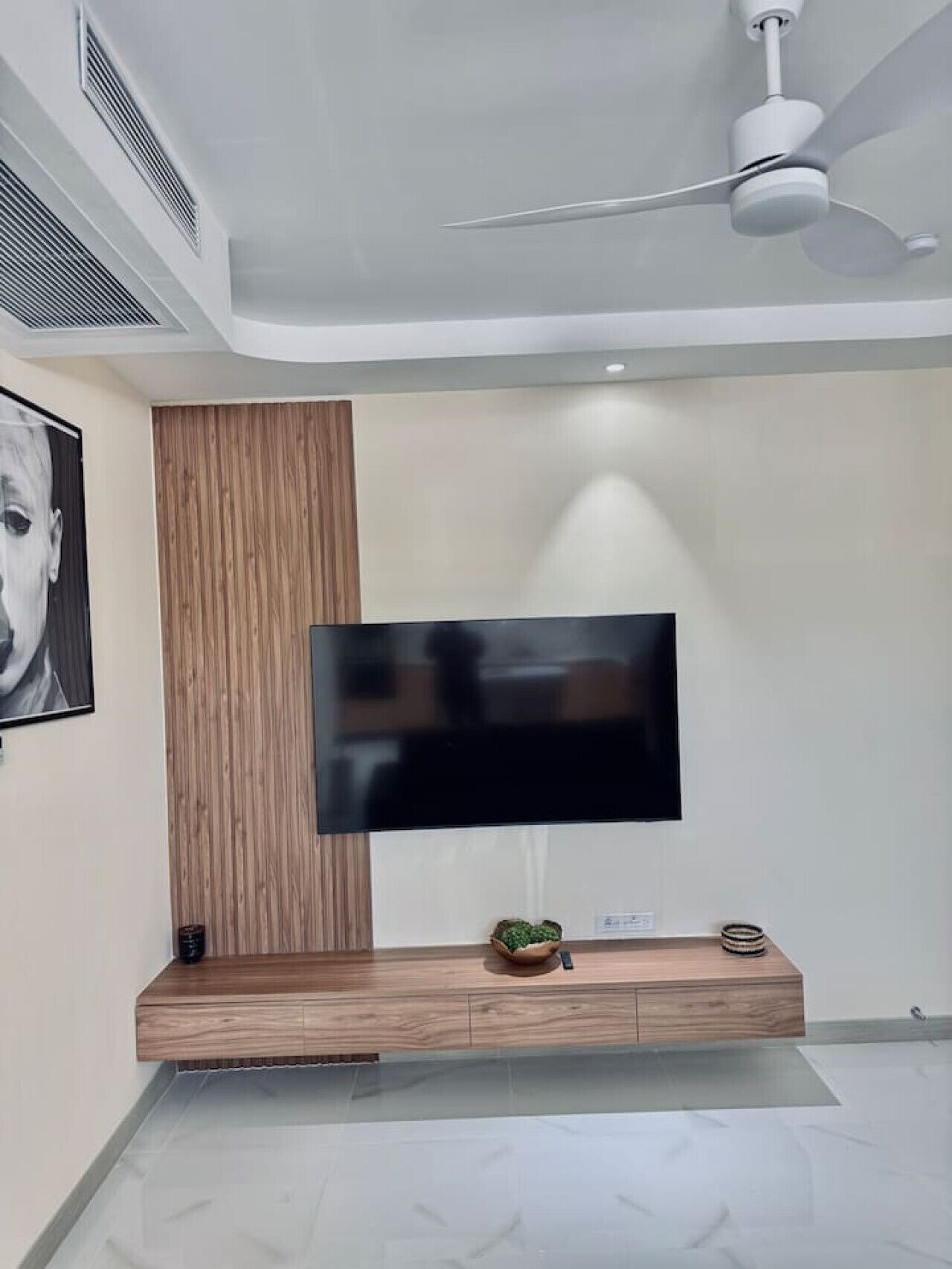 Ein modernes Wohnzimmer mit Wand-Fernseher, Wandverkleidung aus Holzpaneelen und Deckenventilator.