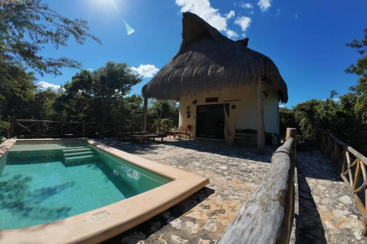 Un edificio con techo de paja, piscina y suelo de piedra.