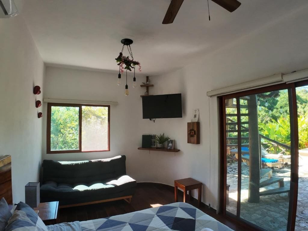 A bedroom with a bed, a sofa, a TV, a window, and a sliding glass door leading to an outdoor area.