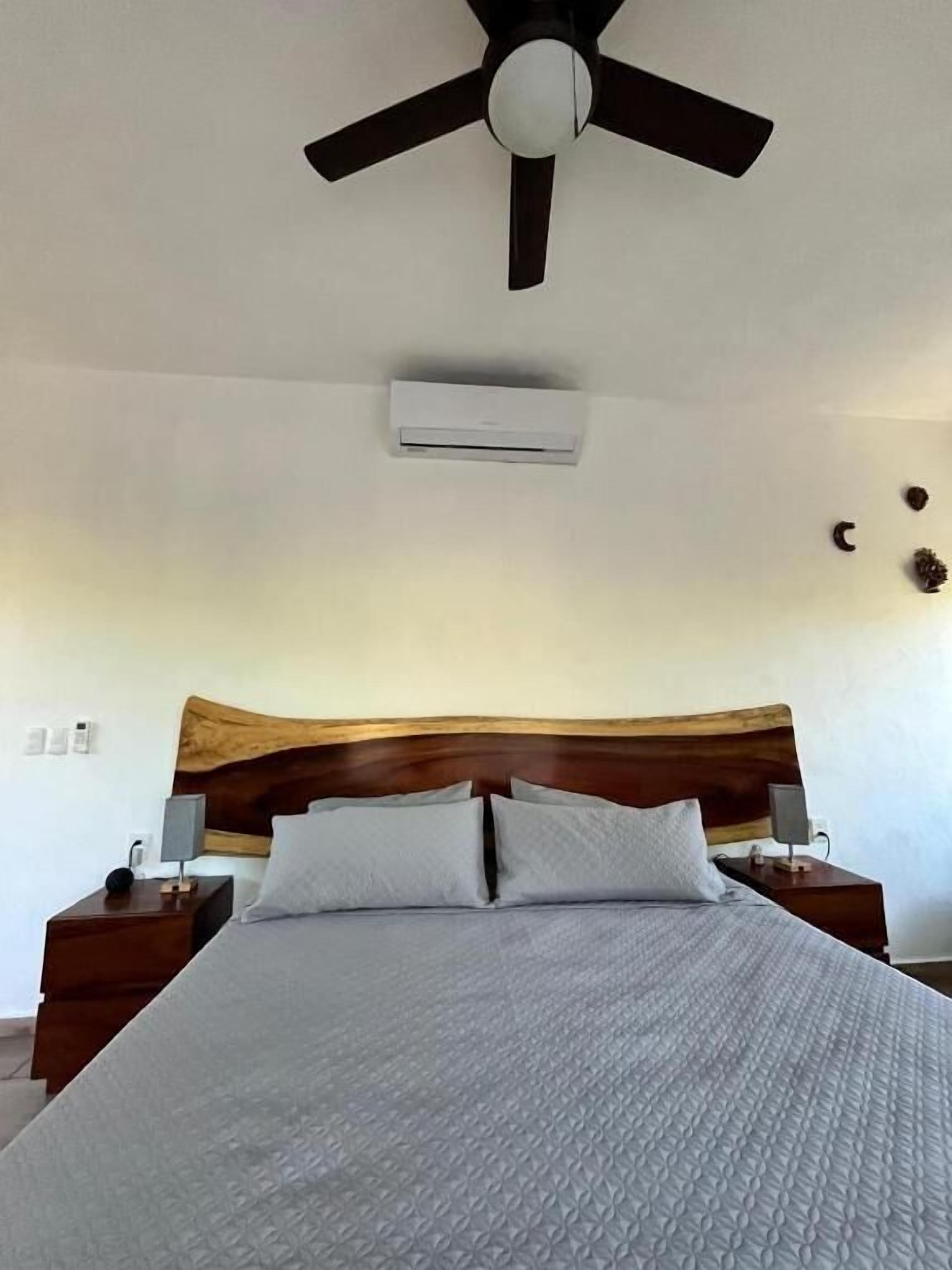 Een hotelkamer met een bed, een houten hoofdbord, nachtkastjes, een plafondventilator en een airconditioning.