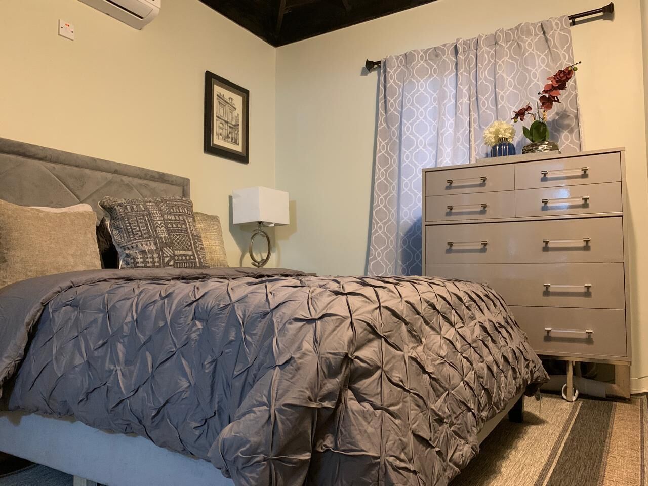 Een slaapkamer met een bed, een dressoir, een nachtkastje en een wandlamp.