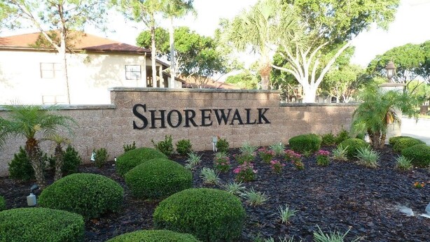 Un cartel que dice 'Shorewalk', con un jardín ajardinado con arbustos bien recortados y árboles pequeños.
