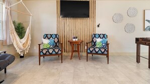 A living room with two patterned armchairs, a small round table, a hammock, a television, and decorative wall art. - Private Heated Pool/Waterfront/5-mins to Beach (Largo)