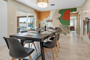 A dining area with a long table set for six, chairs, and a wall with a leaf pattern and the word 'TOWELS' visible.