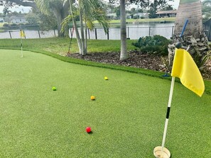 A miniature golf course with a flagstick, a yellow flag, and golf balls on artificial grass.