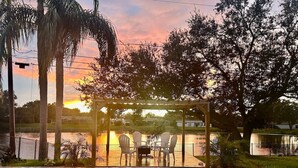 A swimming pool with a covered seating area and chairs, surrounded by trees and a view of a sunset. - Private Heated Pool/Waterfront/5-mins to Beach (Largo)