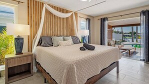A bedroom with a large bed, a nightstand, a lamp, and a view of an outdoor pool area. - Private Heated Pool/Waterfront/5-mins to Beach (Largo)