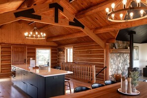 Ein rustikales Blockhaus-Interieur mit einer zentralen Kochinsel, Holzbalkendecke und einem Kamin aus Naturstein.