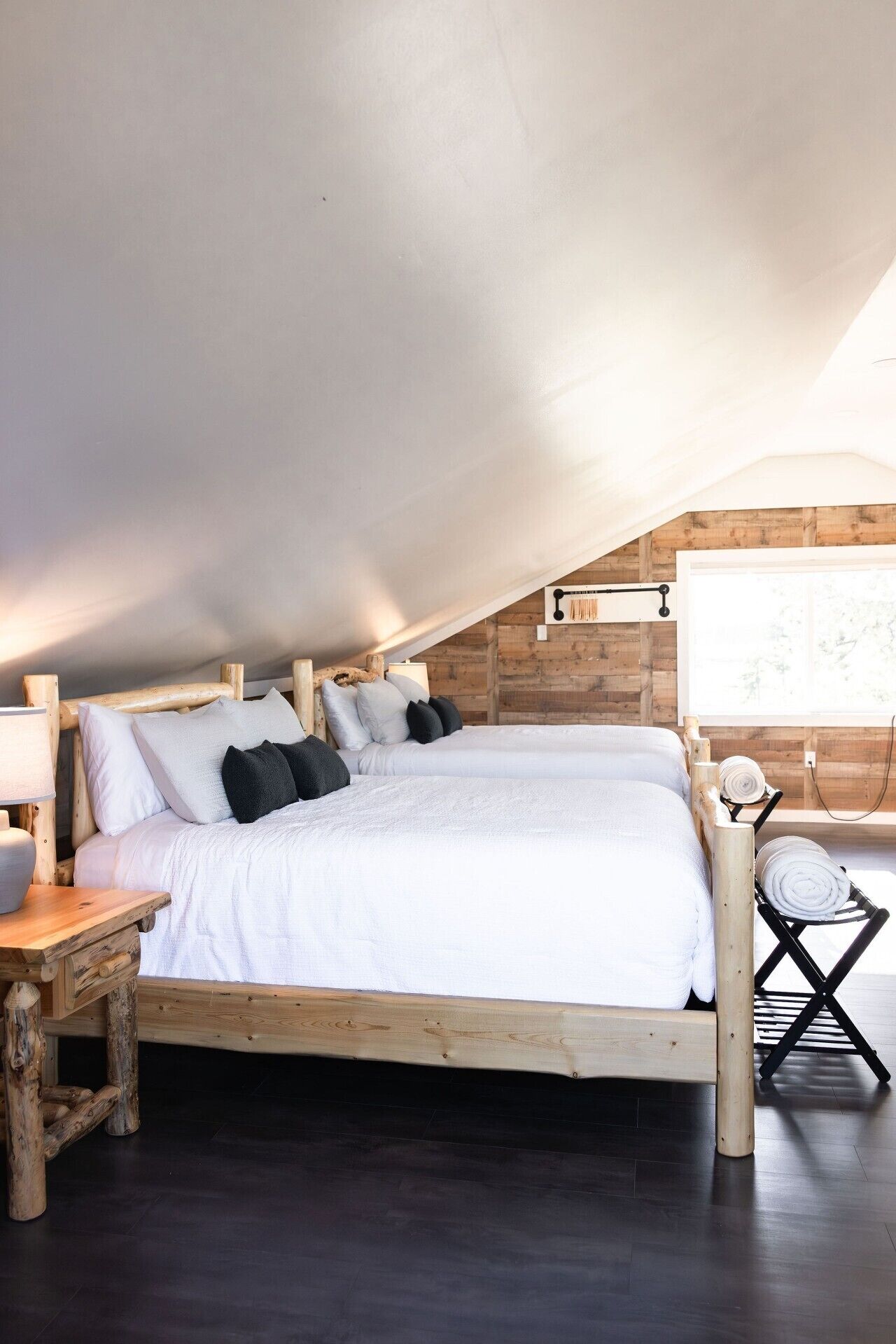 A bedroom with a wooden bed, pillows, a nightstand, and a window with a view.
