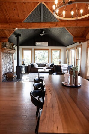 Una habitación amplia con techo de madera, chimenea de piedra, sofá y una mesa de comedor.