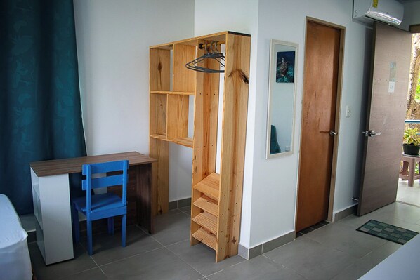 A room with a desk, a blue chair, a wooden shelving unit, a door, and a small potted plant. - Sukha Hippocampus (San Andrés)