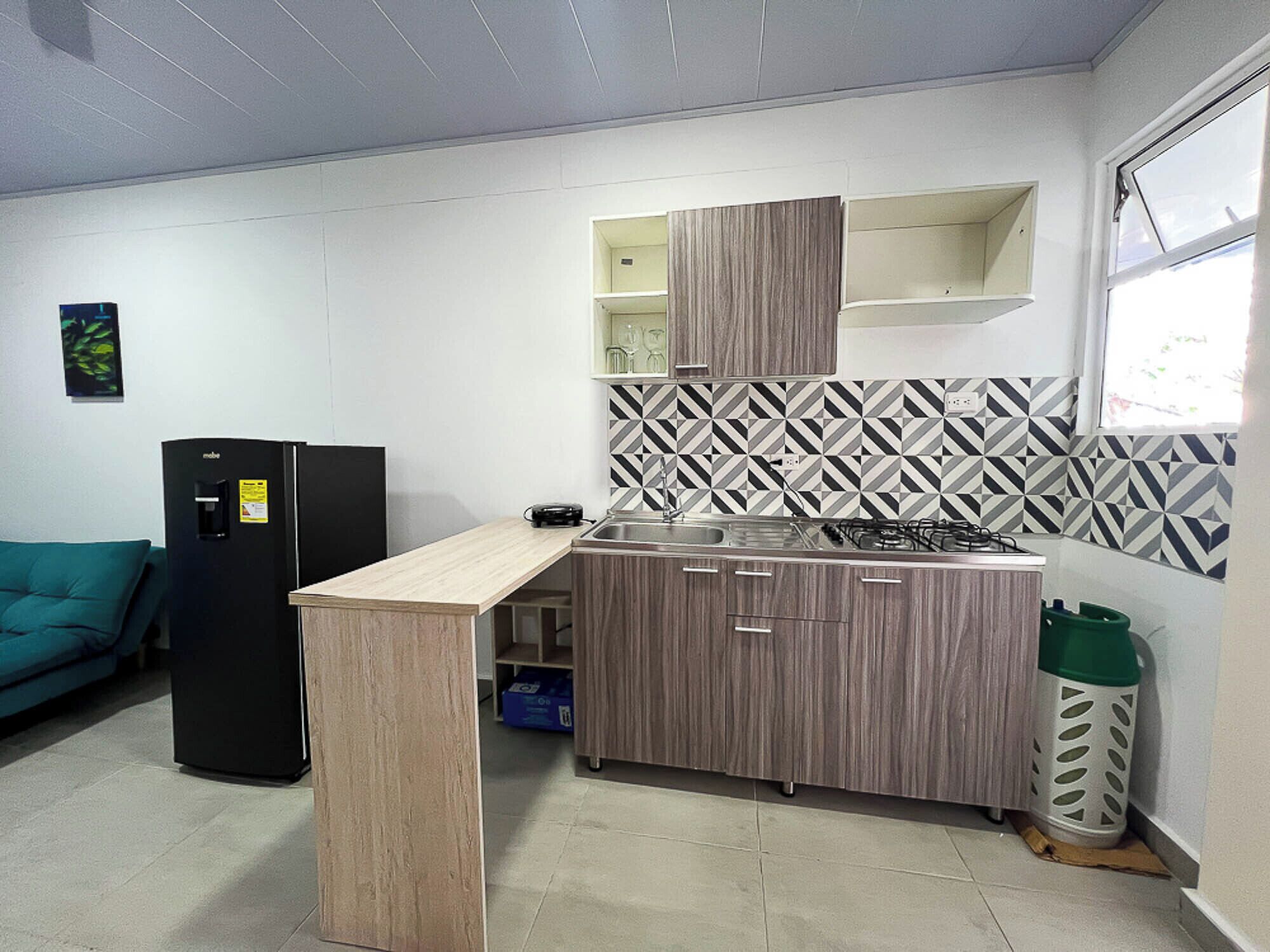 Cocina compacta con estufa integrada, refrigerador y microondas. Cuenta con una ventana que proporciona luz natural y un salpicadero con diseño.