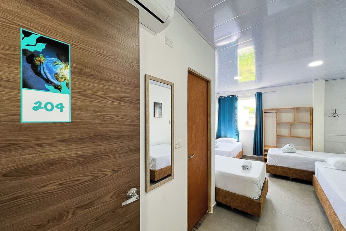A hotel room with two single beds, a wooden wardrobe, a mirror, and a framed picture on the wall.