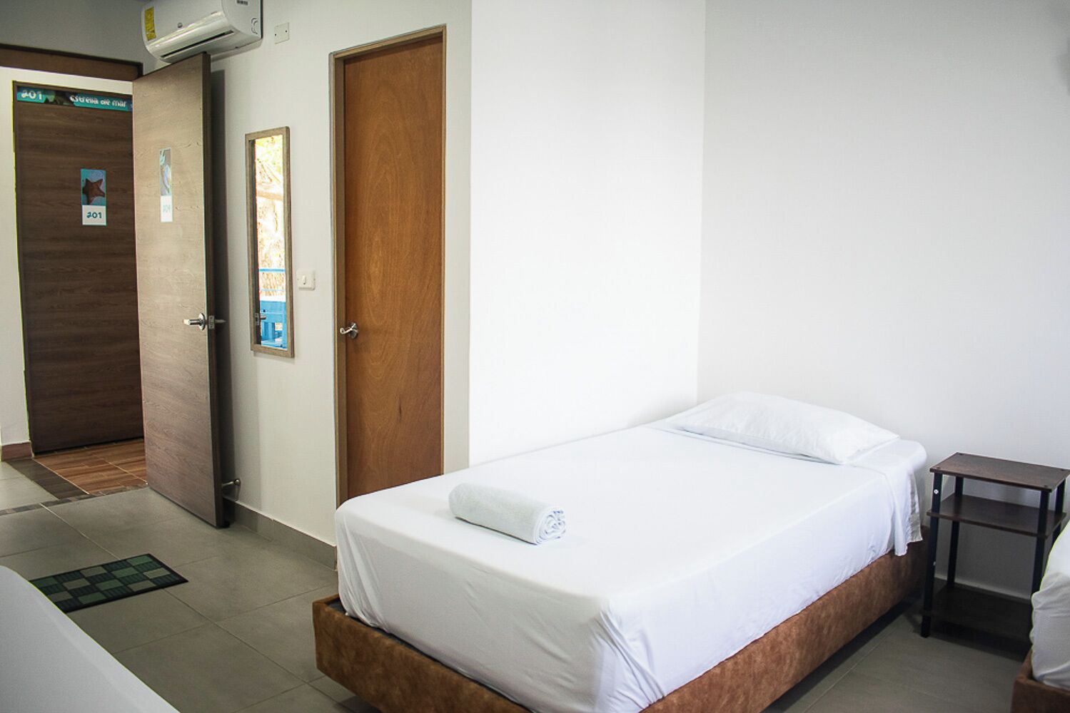 A hotel room with a single bed, a wooden nightstand, a small table, and a door with a sign.