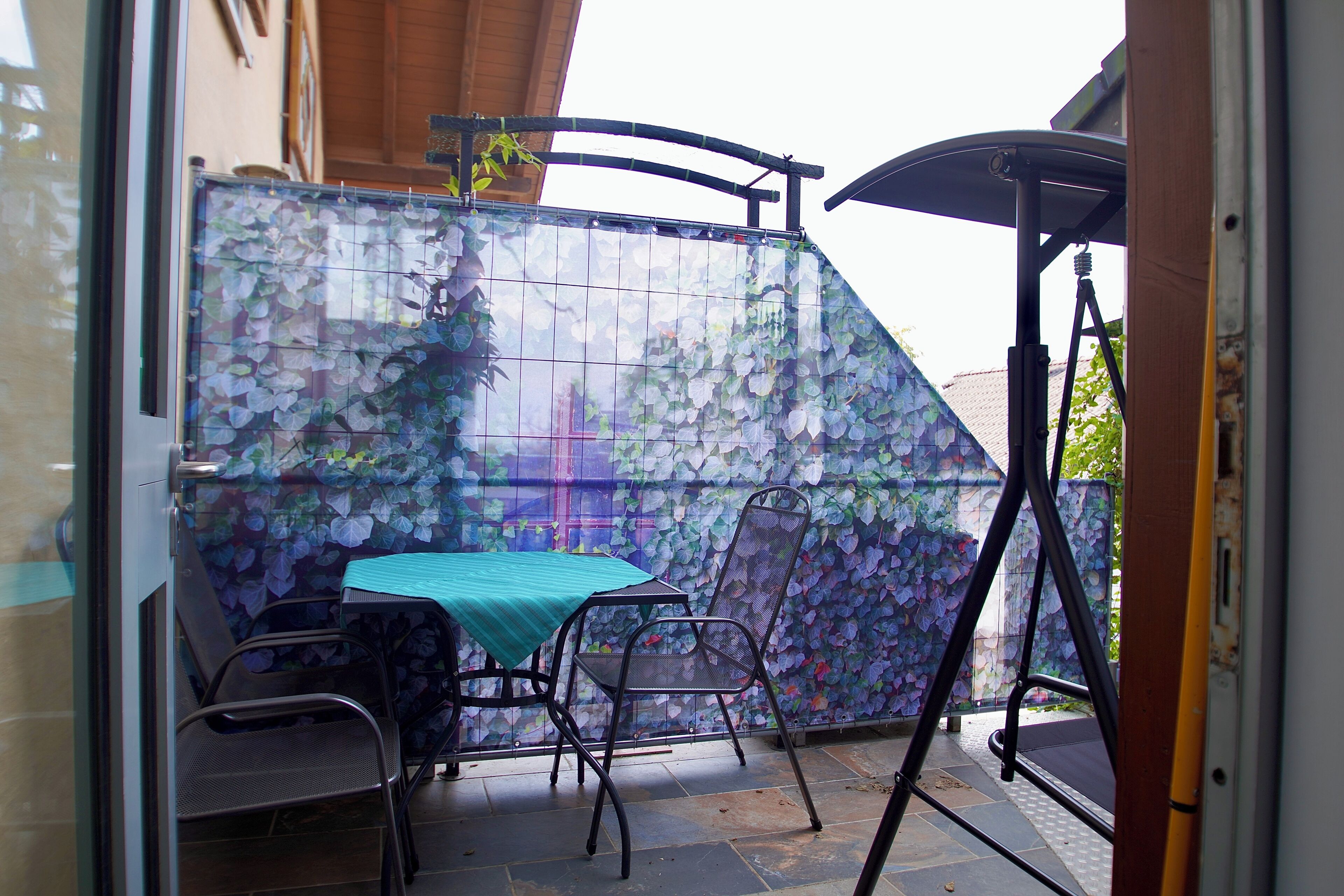 Un'area patio con tavolo e sedie, un elegante parete in vetro e un ombrellone in metallo.