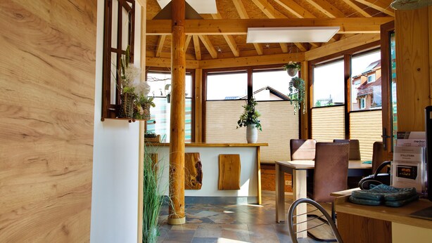 Un intérieur en bois avec un plafond haut, de grandes fenêtres et un coin repas comprenant une table et des chaises.