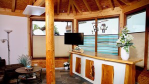 Un intérieur en bois avec un téléviseur posé sur un meuble en bois, une table ronde avec une lampe et une plante en pot.