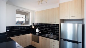 A modern kitchen with black countertops, stainless steel appliances, and light wood cabinets.