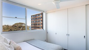 A bedroom with a large window, a bed, a ceiling fan, and a wardrobe.