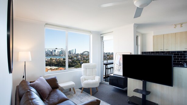 A modern living room with a city view, a flat-screen TV, and a minimalist kitchen.