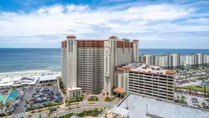 A high-rise hotel with multiple floors, a parking lot, and a view of the ocean. - Beach, Please! (Panama City Beach)