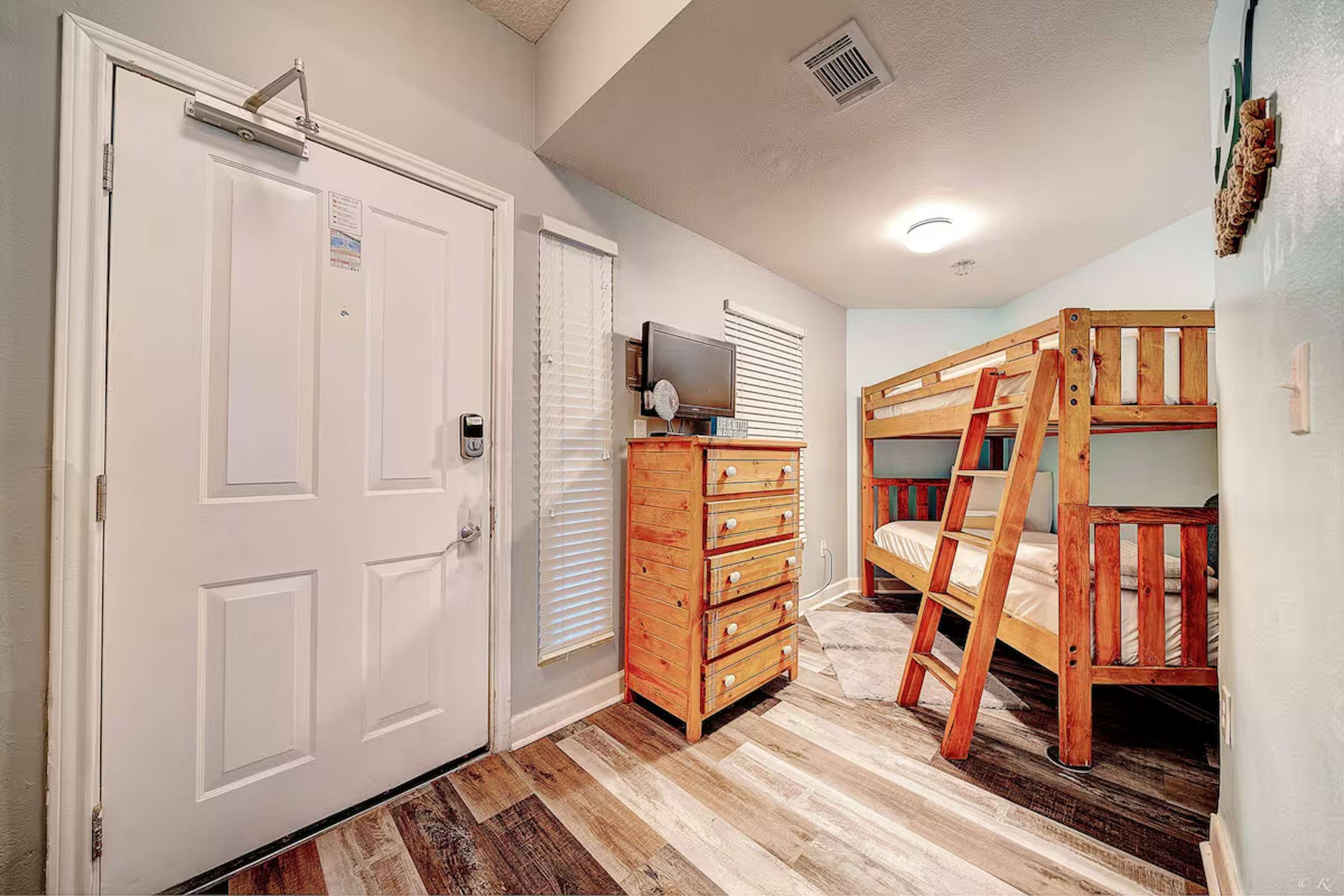 A bedroom with a bunk bed, a wooden dresser, a television, and a door with a mailbox.