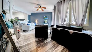 A modern living room with a ceiling fan, a sofa, a coffee table, and a dining area with a table and chairs. - Beach, Please! (Panama City Beach)