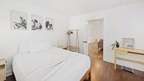 A modern bedroom with a large bed, a wooden bedside table, a desk, and a chair. There are three framed artworks on the wall and a door leading to another room. - Chef's Kitchen; 2 King Beds with 55" TV's & Bunk Bed, 70" TV in Living Room (Atlanta)