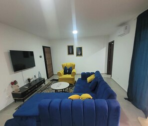 A living room with a blue sofa, a yellow armchair, a flat-screen TV, and a small table.