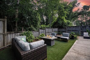 A backyard with a wooden fence, a grassy lawn, and outdoor furniture including a wicker sofa and two chairs.