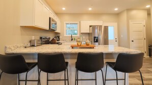 A modern kitchen with a large island, black bar stools, stainless steel appliances, and a window providing natural light. - 3BR Condo Near Ripken Experience & LeConte Center (Pigeon Forge)
