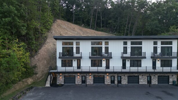 A modern two-story building with multiple balconies and large windows, surrounded by dense forest. - 3BR Condo Near Ripken Experience & LeConte Center (Pigeon Forge)